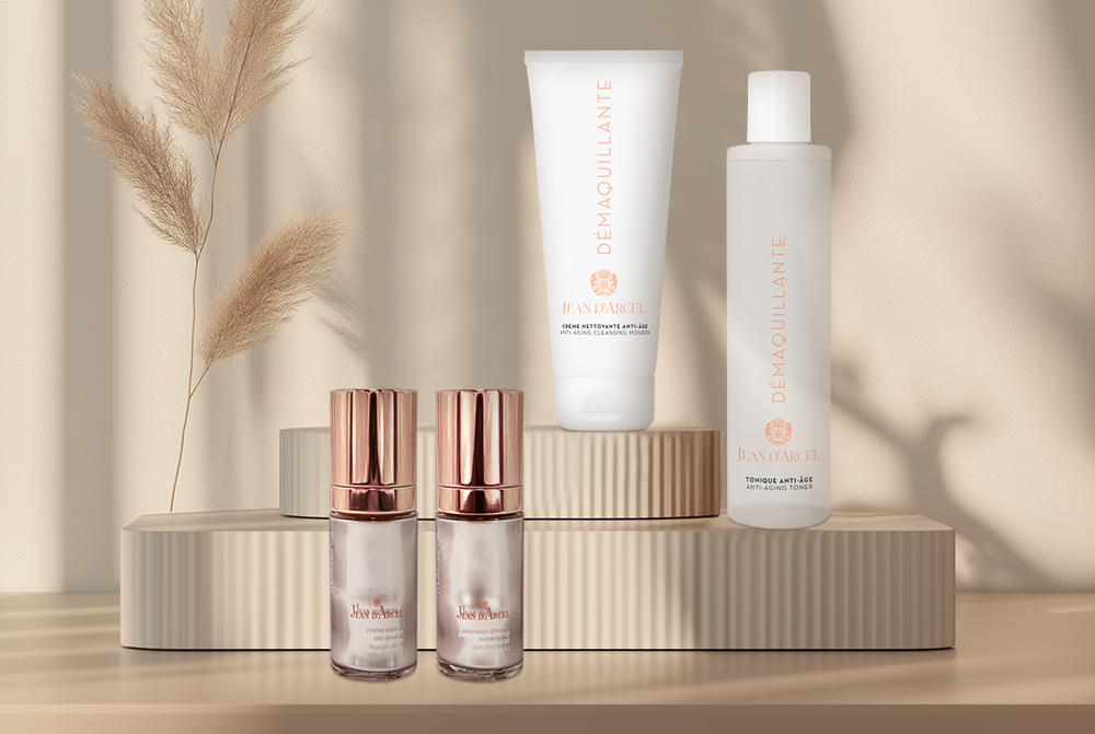 JEAN D'ARCEL Pflegeprodukte auf Podesten mit dekorativem Pampasgras.